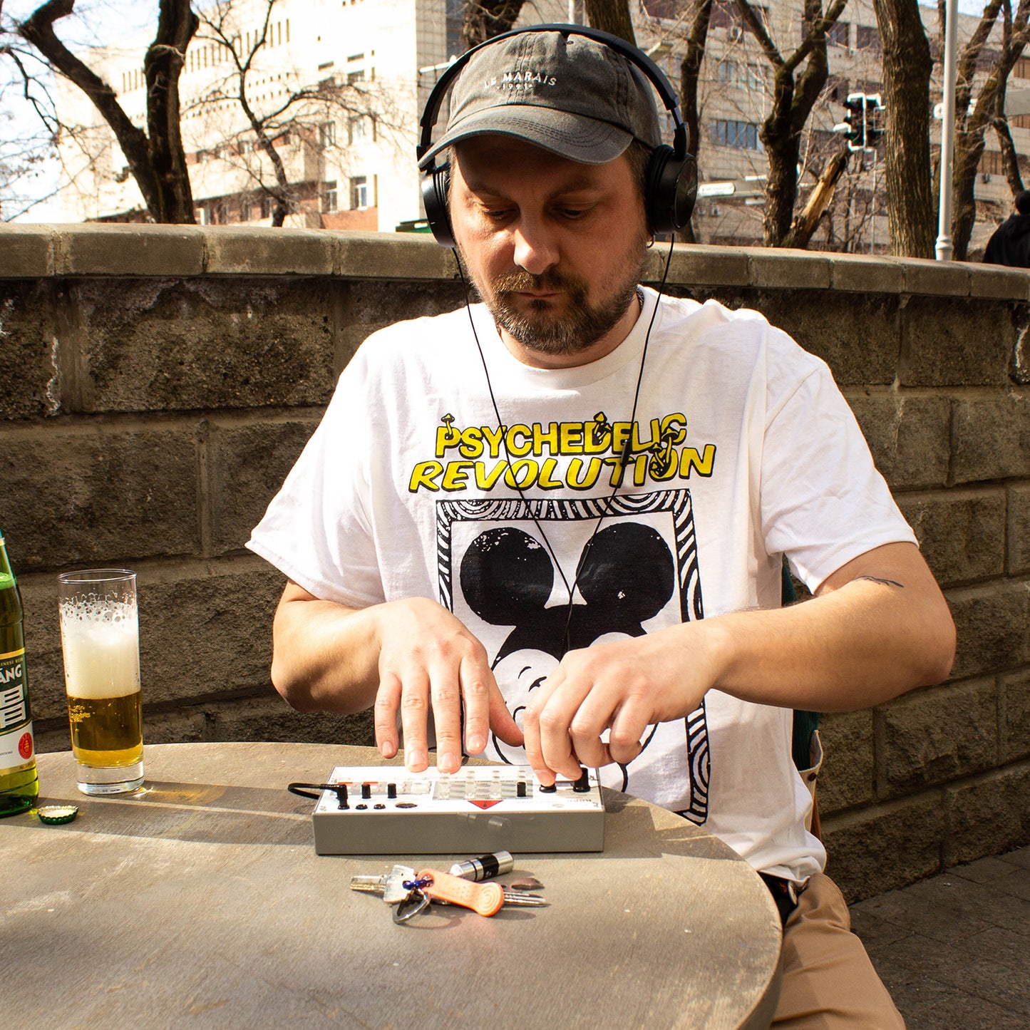 Man wearing Psychedelic Revolution T-Shirt outdoors at cafe table mixing on portable synth with beer